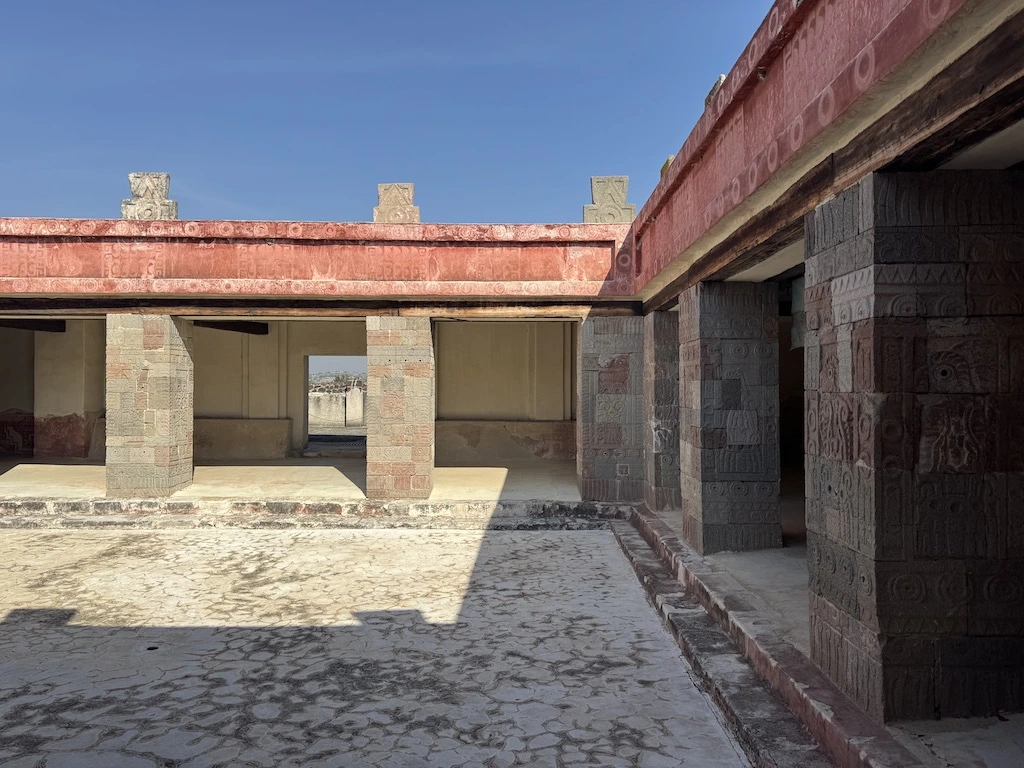 Sunlit courtyard with painted red stone columns and carved motifs at the Palace of Quetzalpapálotl in Teotihuacan